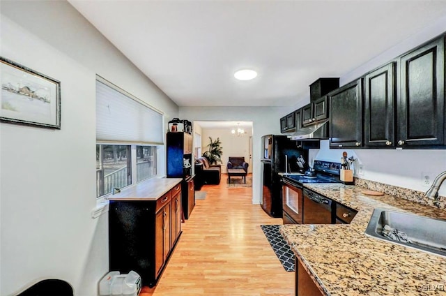 kitchen featuring sink, light hardwood / wood-style floors, light stone countertops, black appliances, and a notable chandelier