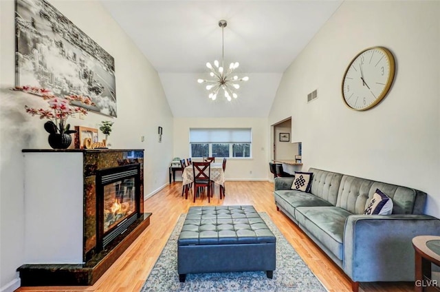 living room with wood-type flooring, a tiled fireplace, vaulted ceiling, and a notable chandelier