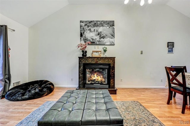 living area featuring a high end fireplace, vaulted ceiling, and hardwood / wood-style flooring