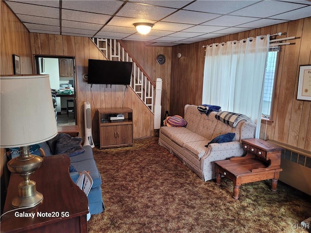 carpeted living room featuring a paneled ceiling and wood walls