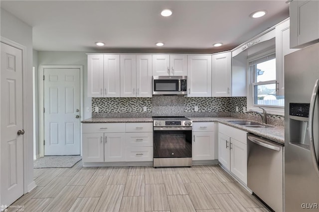 kitchen with appliances with stainless steel finishes, white cabinets, light stone counters, and sink