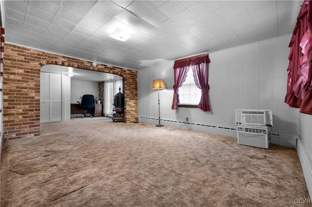 carpeted empty room featuring baseboard heating, a wall mounted AC, and brick wall