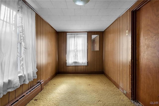 carpeted spare room with wooden walls and a baseboard radiator