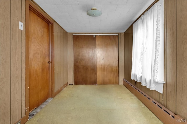 hallway featuring wooden walls, a baseboard heating unit, and light carpet