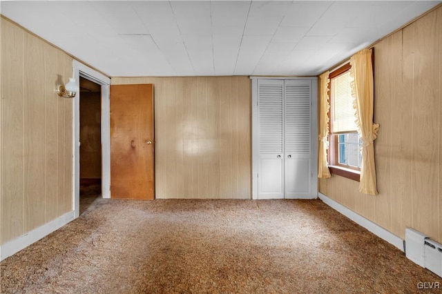 unfurnished bedroom with wooden walls, carpet floors, and a baseboard heating unit