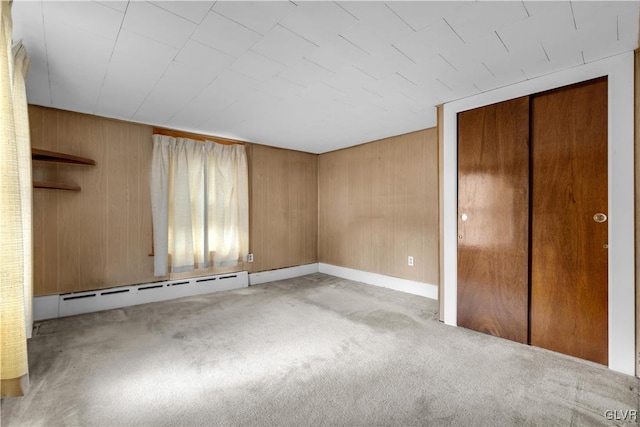 unfurnished bedroom with baseboard heating, light carpet, a closet, and wood walls