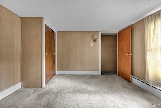 carpeted empty room with a baseboard radiator and wooden walls