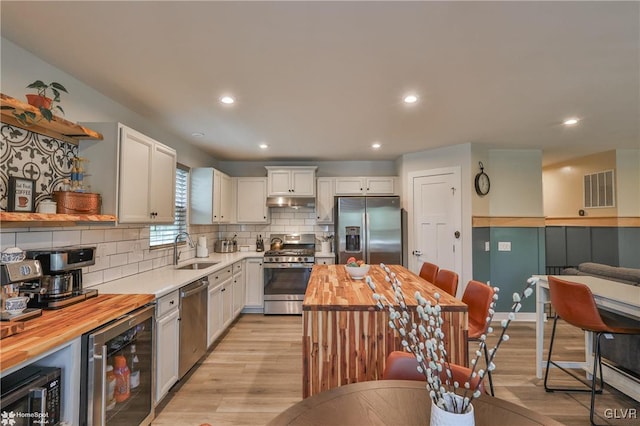 kitchen featuring beverage cooler, wood counters, white cabinetry, appliances with stainless steel finishes, and sink