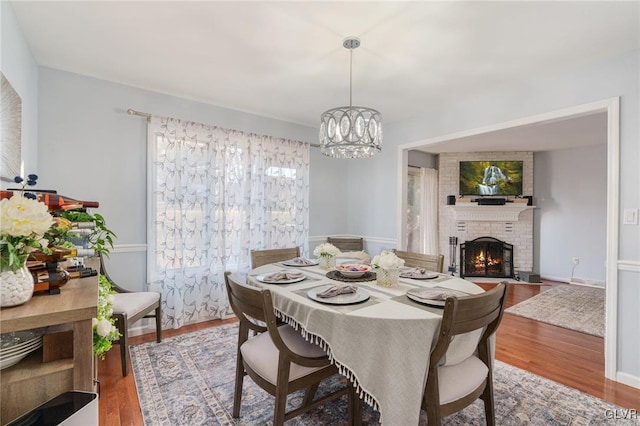 dining room with a brick fireplace, a chandelier, and wood-type flooring