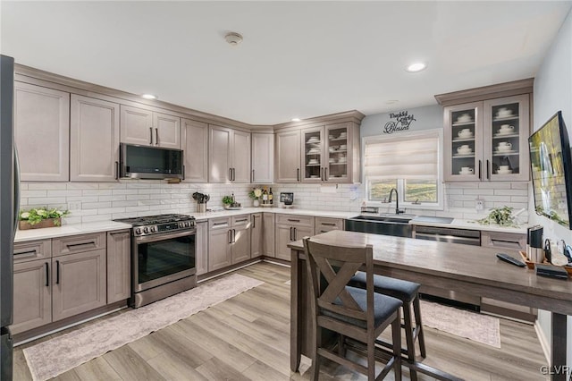 kitchen with sink, light wood-type flooring, tasteful backsplash, and appliances with stainless steel finishes