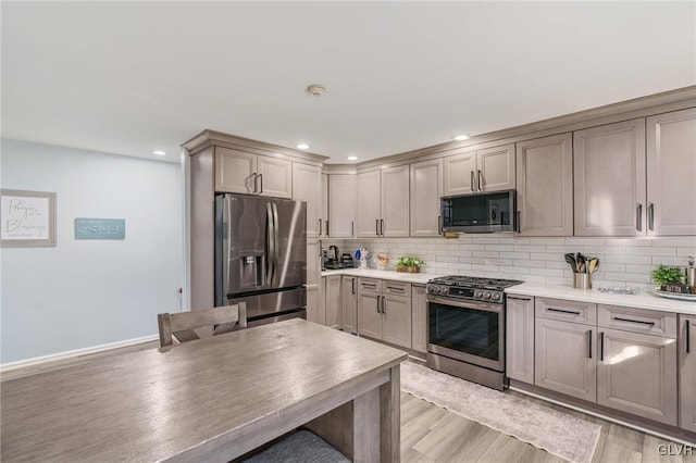 kitchen featuring appliances with stainless steel finishes, light hardwood / wood-style flooring, gray cabinetry, and decorative backsplash