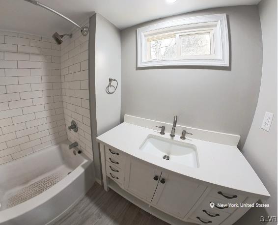 bathroom with wood-type flooring, vanity, and tiled shower / bath