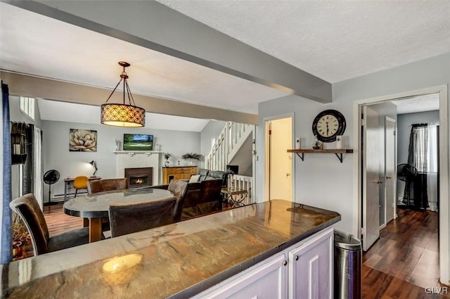 kitchen with a brick fireplace, beam ceiling, hanging light fixtures, dark wood-type flooring, and a textured ceiling