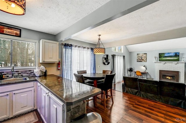 kitchen featuring kitchen peninsula, dark hardwood / wood-style flooring, a fireplace, a textured ceiling, and sink