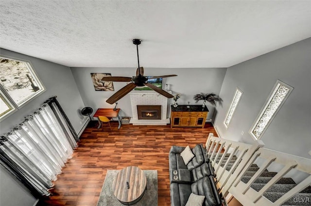 living room featuring a textured ceiling, ceiling fan, dark hardwood / wood-style floors, and a brick fireplace