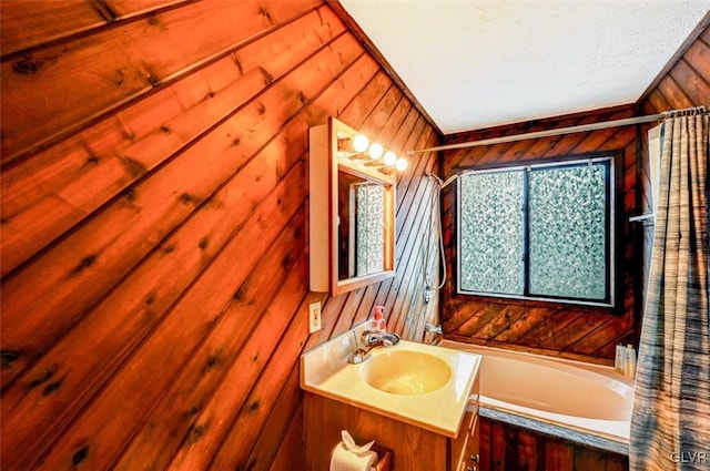 bathroom featuring a tub to relax in, vanity, wood walls, and a textured ceiling