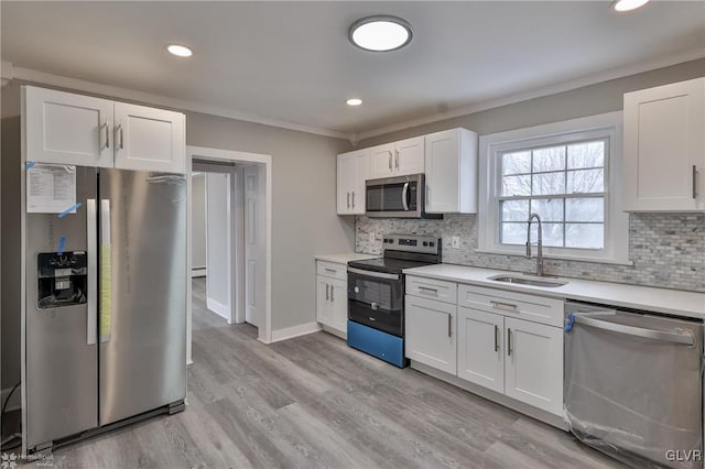 kitchen featuring appliances with stainless steel finishes, white cabinetry, tasteful backsplash, sink, and light hardwood / wood-style flooring