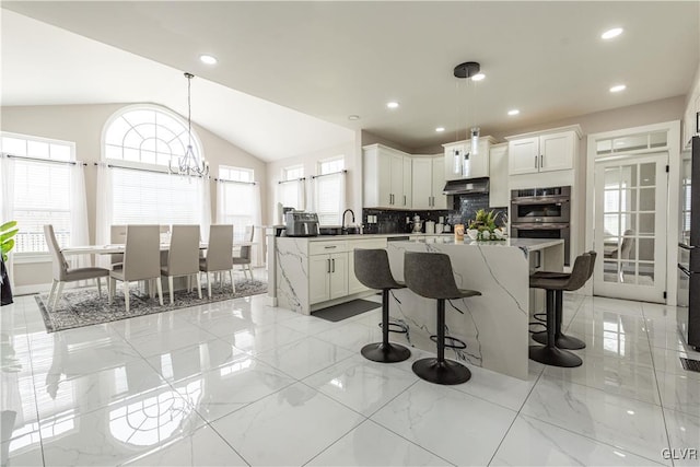 kitchen featuring a kitchen island, decorative light fixtures, white cabinetry, double oven, and backsplash