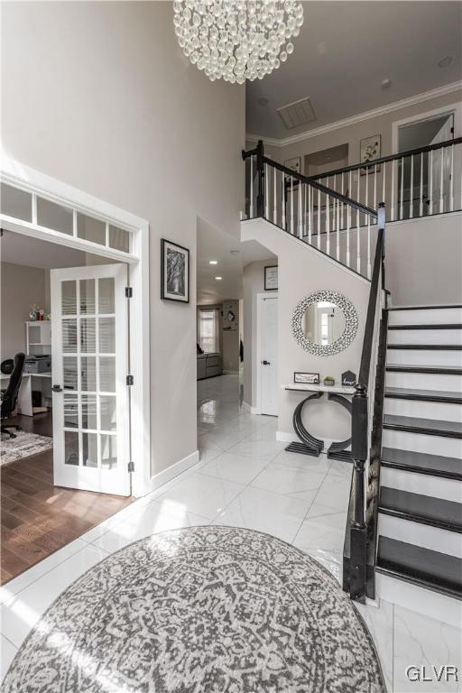 foyer featuring a towering ceiling, ornamental molding, and a chandelier