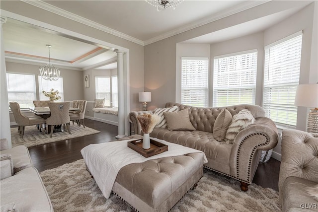 living room with a wealth of natural light, dark hardwood / wood-style flooring, an inviting chandelier, decorative columns, and crown molding