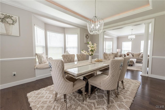 dining space featuring a notable chandelier, a raised ceiling, dark wood-type flooring, ornamental molding, and ornate columns