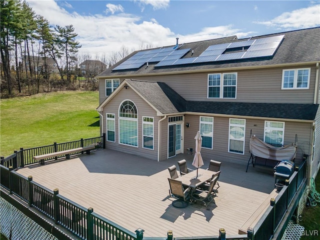 rear view of property featuring a deck, a yard, and solar panels