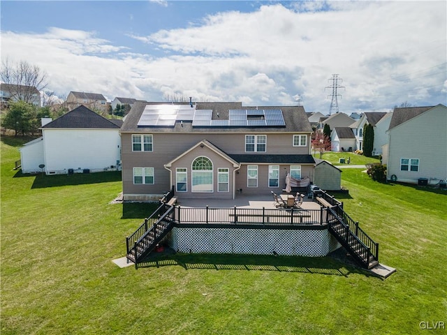 rear view of house featuring a patio area, a deck, a lawn, and solar panels