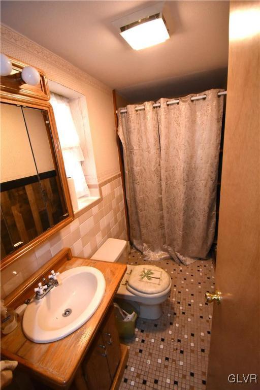 bathroom featuring toilet, vanity, tile walls, walk in shower, and tile patterned flooring