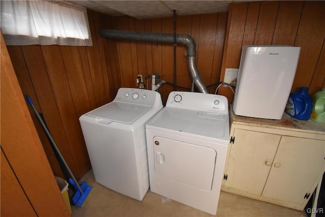 clothes washing area featuring cabinets, washer and clothes dryer, and wooden walls