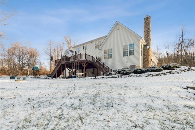 snow covered rear of property with a playground and a wooden deck