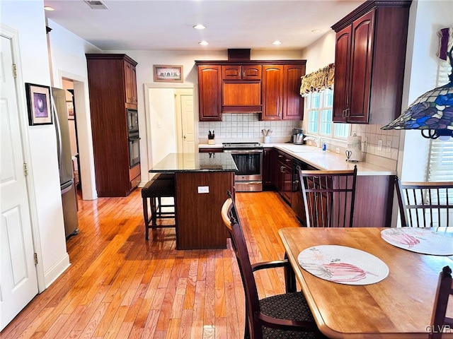 kitchen with black appliances, a kitchen island, light hardwood / wood-style floors, decorative backsplash, and a breakfast bar