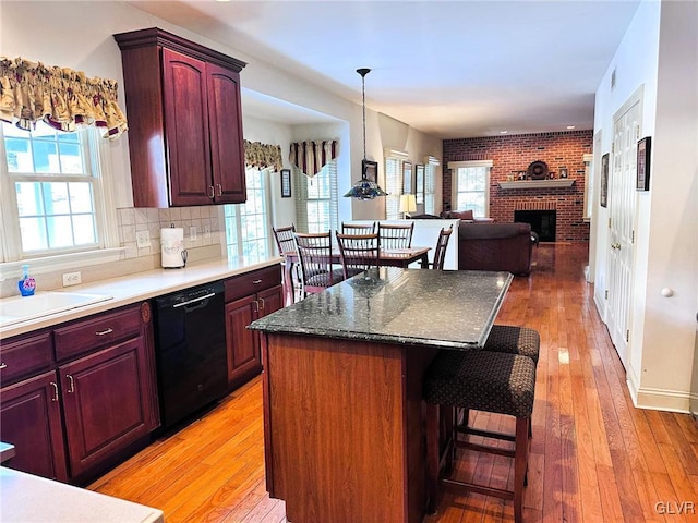 kitchen featuring a brick fireplace, black dishwasher, backsplash, light hardwood / wood-style flooring, and a breakfast bar