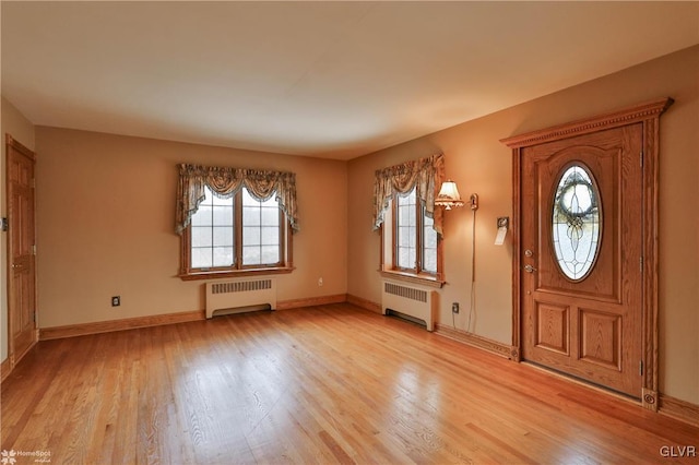 foyer entrance featuring a wealth of natural light, radiator heating unit, and light hardwood / wood-style flooring