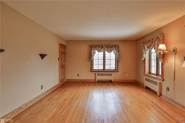 spare room featuring radiator, light wood-type flooring, and a healthy amount of sunlight