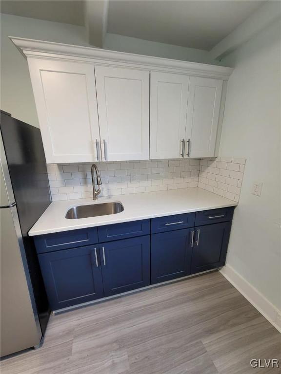 kitchen featuring decorative backsplash, sink, blue cabinetry, white cabinets, and stainless steel fridge