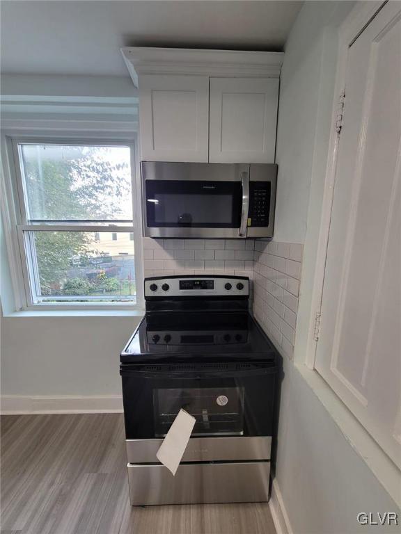 kitchen with light wood-type flooring, stainless steel appliances, decorative backsplash, and white cabinets