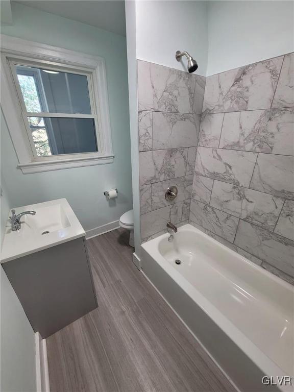 full bathroom with hardwood / wood-style flooring, toilet, vanity, and tiled shower / bath