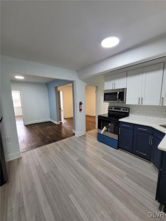 kitchen with tasteful backsplash, electric range, white cabinetry, and light hardwood / wood-style flooring