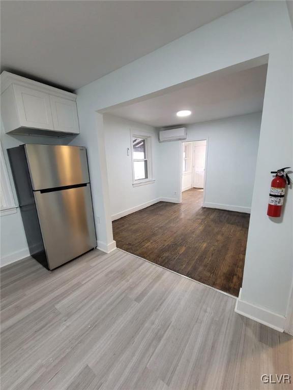 kitchen featuring light hardwood / wood-style flooring, white cabinets, stainless steel fridge, and a wall unit AC