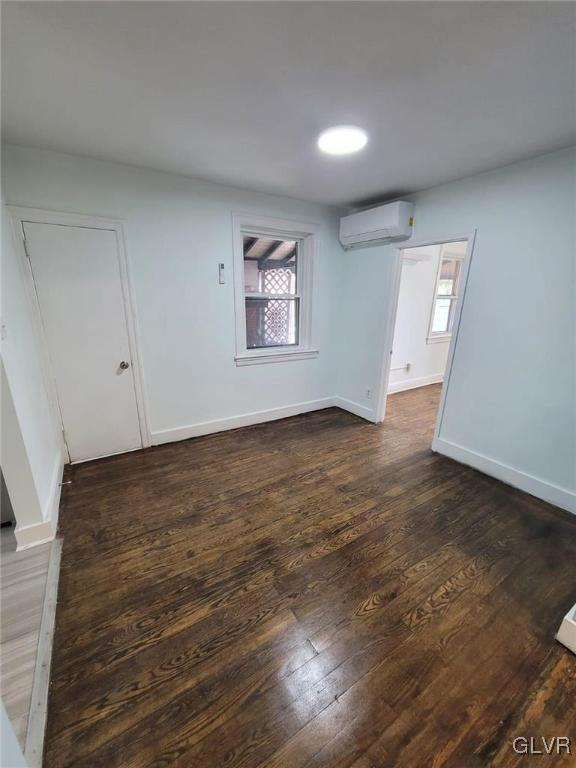 empty room with dark hardwood / wood-style floors and a wall unit AC