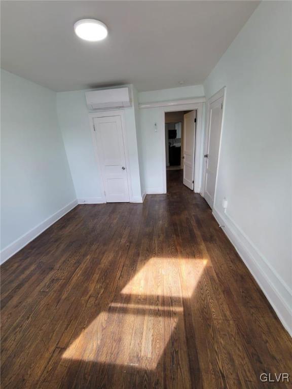 spare room featuring dark hardwood / wood-style flooring and a wall unit AC