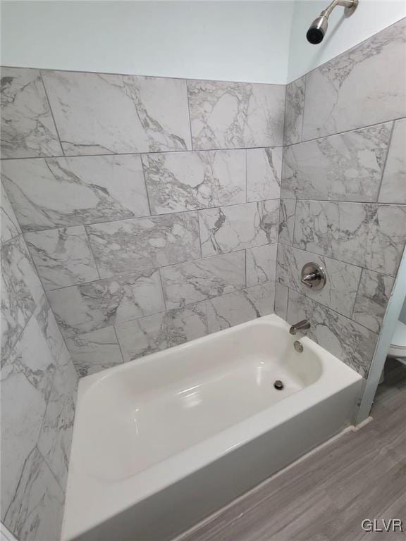 bathroom featuring wood-type flooring, toilet, and tiled shower / bath