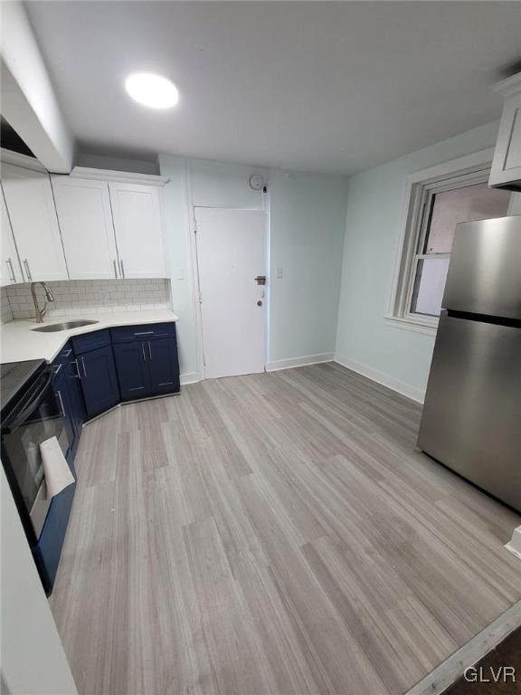 kitchen with backsplash, blue cabinets, stainless steel refrigerator, white cabinets, and sink