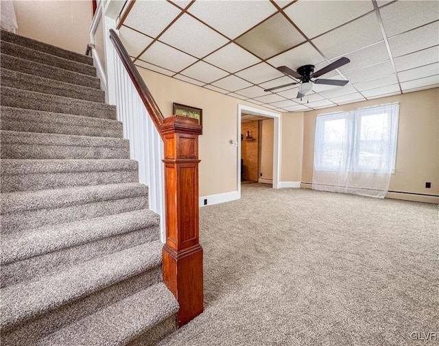 stairs featuring ceiling fan, a drop ceiling, a baseboard heating unit, and carpet