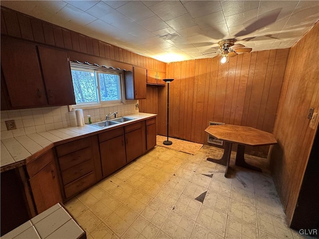 kitchen featuring ceiling fan, wooden walls, sink, and tile countertops