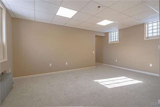 basement featuring radiator, a drop ceiling, and light colored carpet