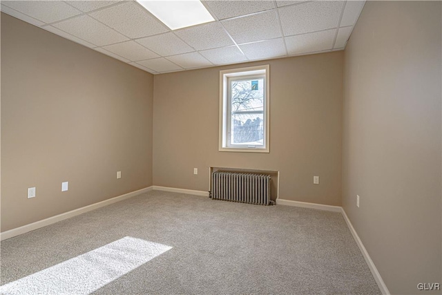 unfurnished room featuring carpet, radiator, and a drop ceiling