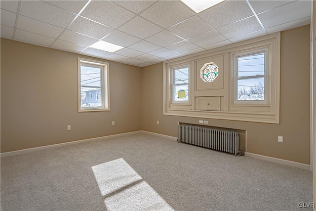 carpeted empty room with a paneled ceiling, a wealth of natural light, and radiator heating unit