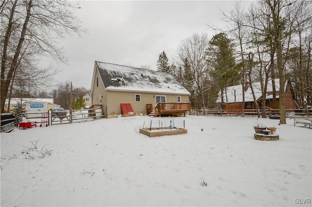 snow covered rear of property with a wooden deck and an outdoor fire pit