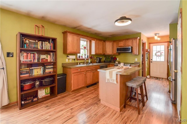 kitchen featuring a kitchen island, stainless steel appliances, sink, light wood-type flooring, and a breakfast bar